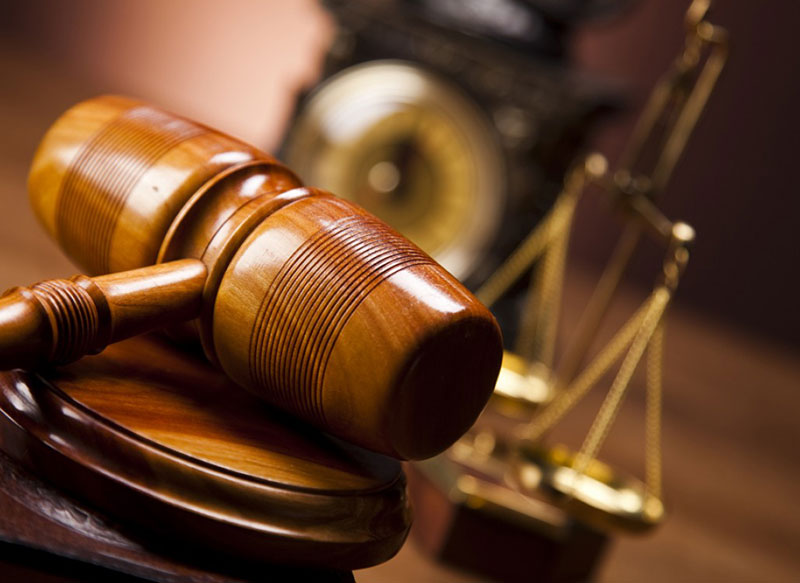 Judge's gavel sitting on desk with clock and justice scales